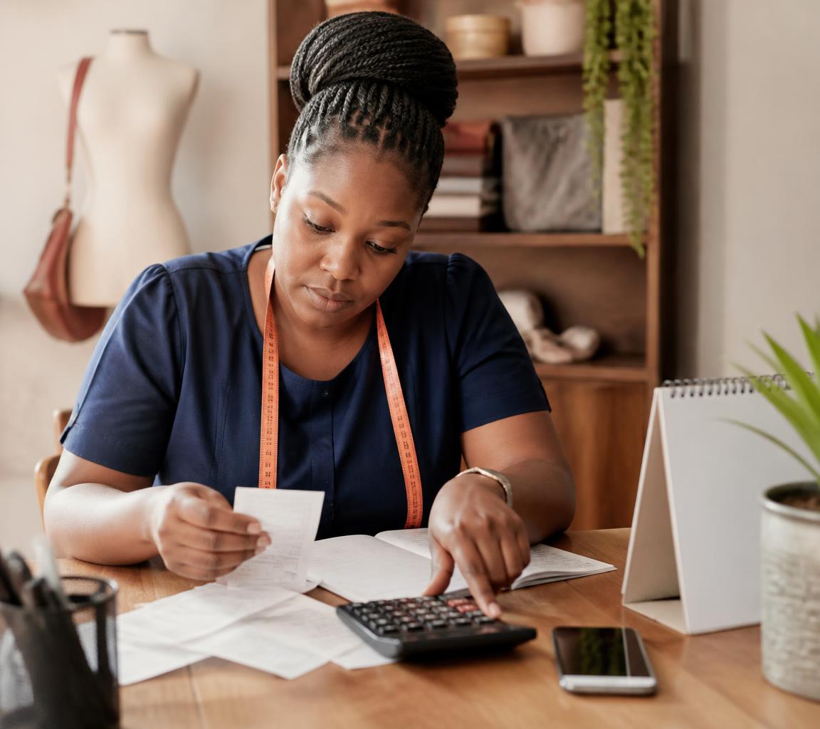 Tanzanian business owner reviewing receipts, a calculator and tax documents at her desk